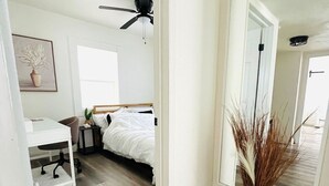 Ein Schlafzimmer mit Bett, Schreibtisch und Stuhl. Eine Deckenventilator und ein Spiegel sind an der Wand angebracht.