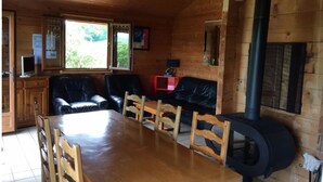 A wooden cabin interior with a dining table, chairs, a sofa, a fireplace, and a window with a view of greenery. - Chalet in the heart of nature near a farm with animals (Lent)