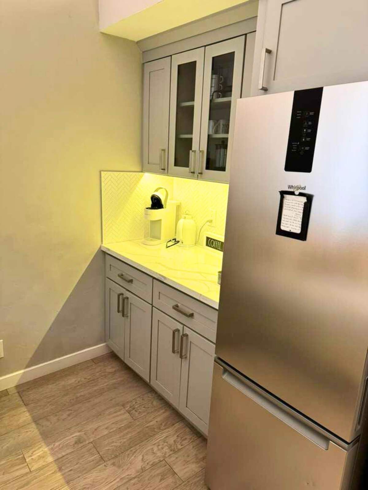 A compact kitchen with a stainless steel refrigerator, a yellow countertop, and grey cabinets.