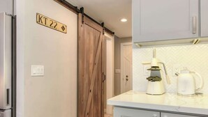 A modern kitchen with light grey cabinets, a stainless steel refrigerator, and a wooden barn-style door.