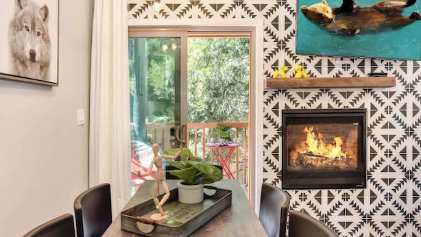 A dining area with a wooden table, chairs, a fireplace, and a patterned wall.