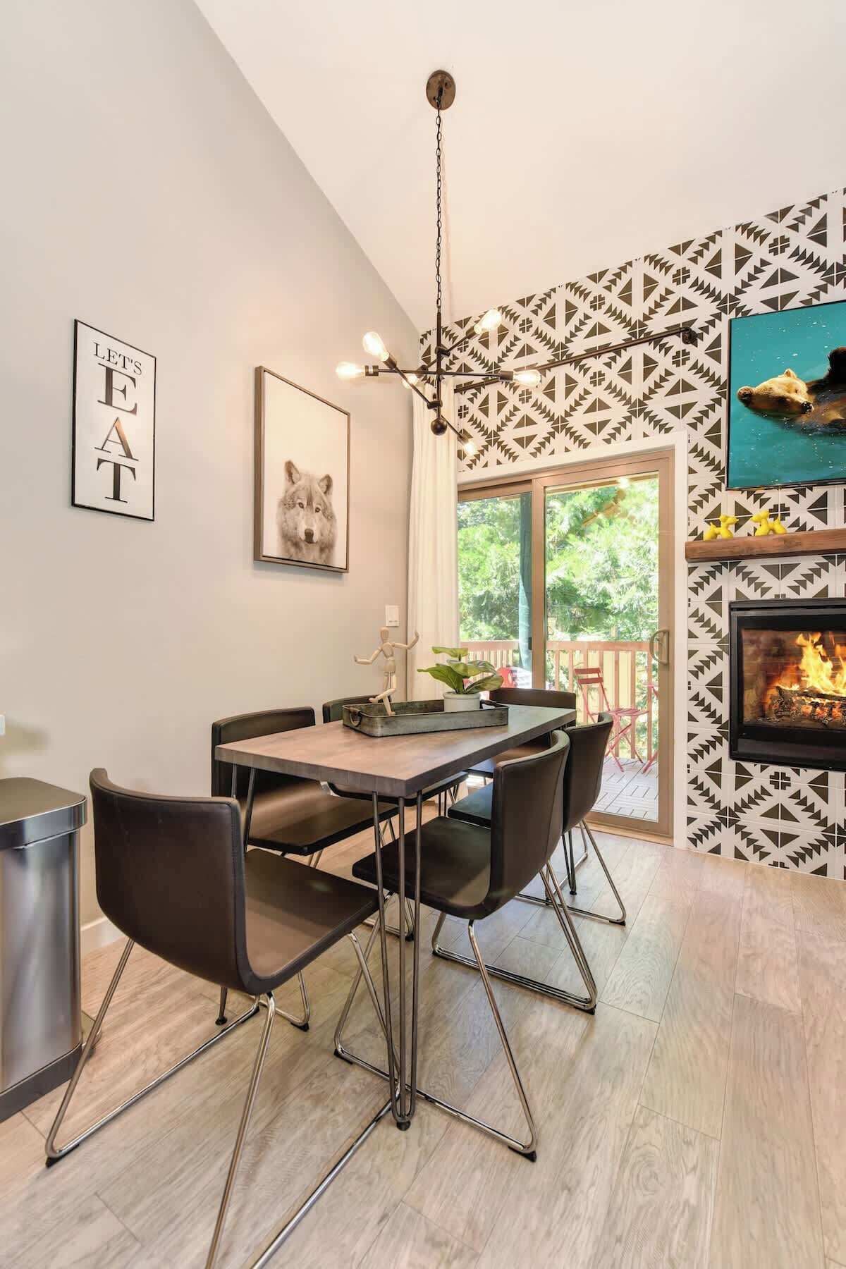 A modern dining area with a wooden table and black chairs, a hanging light fixture, and a patterned wall.