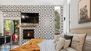 A modern bedroom with a fireplace, a TV mounted on the wall, and a bed with striped bedding.