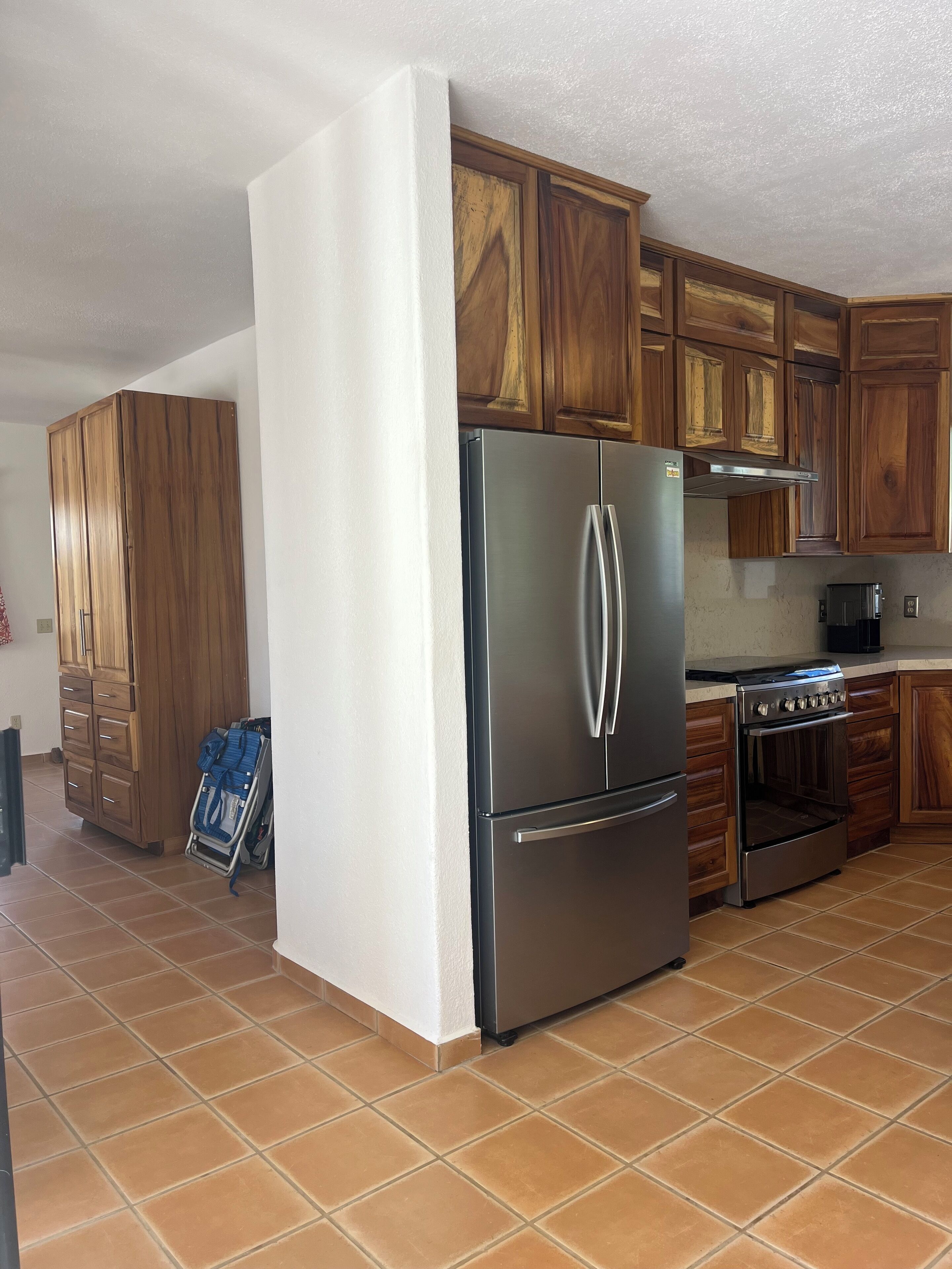 A kitchen with wooden cabinets, a stainless steel refrigerator, an oven, and a tiled floor.