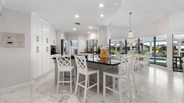 A modern kitchen with white cabinetry, a marble floor, and a dining area with white chairs.