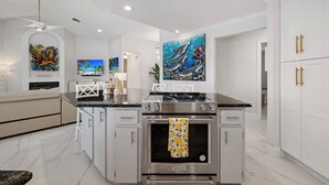 A modern kitchen with white cabinetry, a central island with a stove, and artwork on the walls.