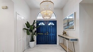 A hallway with a blue door, a potted plant, a console table, and a chandelier.