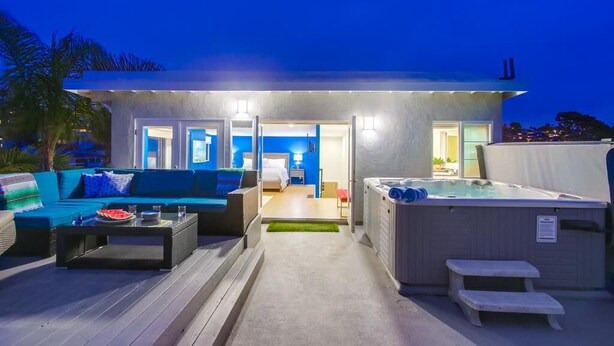 A modern outdoor living area with a hot tub, a sofa, and a dining table.