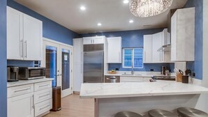 A modern kitchen with white cabinets, a large island with stools, stainless steel appliances, and a chandelier.