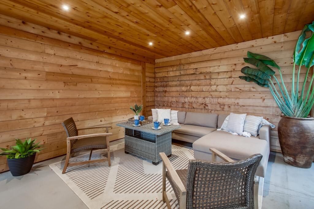 A cozy room with wooden walls, a sofa, two chairs, a small table with blue cups, and a large potted plant.