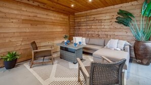 A cozy room with wooden walls, a sofa, two chairs, a small table with blue cups, and a large potted plant.