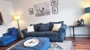 A living room with a dark blue sofa, a matching ottoman, a patterned rug, and a floor lamp. - 2-bedroom townhome in enjoyable Charlotte with WiFi, AC (Charlotte)
