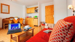 Una sala de estar acogedora con un sofá rojo, una mesa de centro de madera con una computadora portátil, un oso de peluche y una revista.