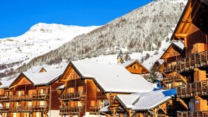 Un conjunto de cabañas de madera con balcones, con una imponente montaña nevada al fondo.