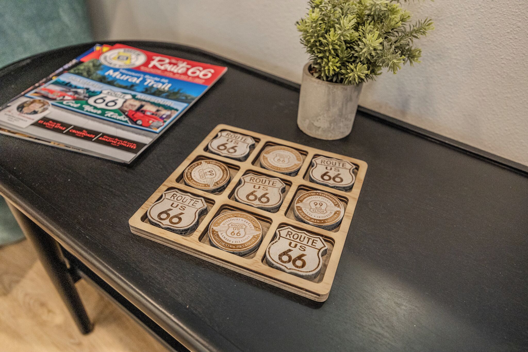 A table with a Route 66-themed board game, a magazine, and a small potted plant.