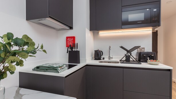 A modern kitchen with dark cabinets, a microwave, a sink, and a countertop with a kettle and a coffee maker. - Manchester City Studio (Manchester)