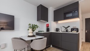 Eine moderne Küche mit dunklen Schränken, einer weißen Arbeitsplatte und einer eingebauten Mikrowelle. Ein kleiner Tisch mit zwei Stühlen und einem Blumentopf stehen darin.