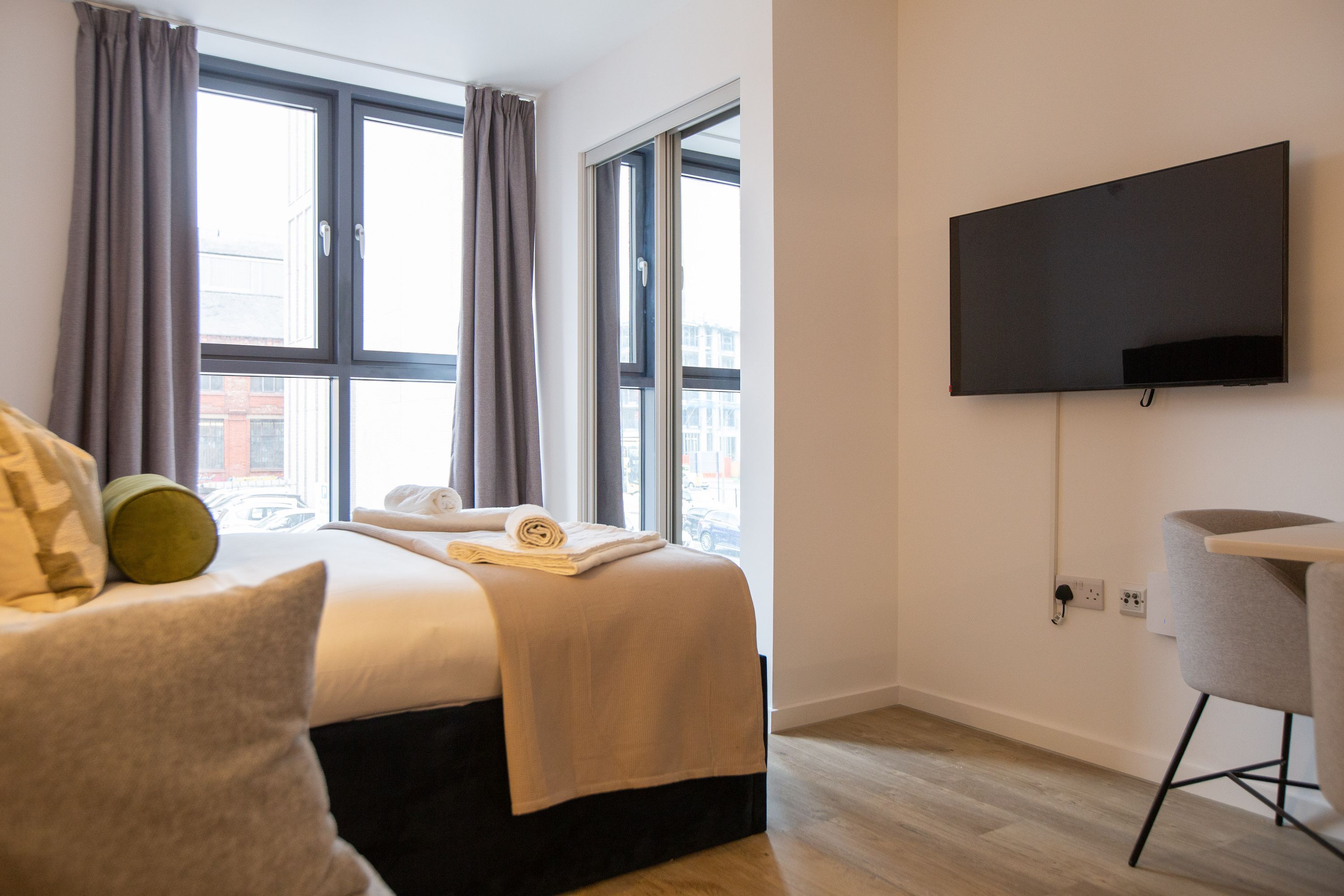 Une chambre d’hôtel avec un lit, un téléviseur à écran plat fixé au mur, une fenêtre avec des rideaux et un plancher en bois.