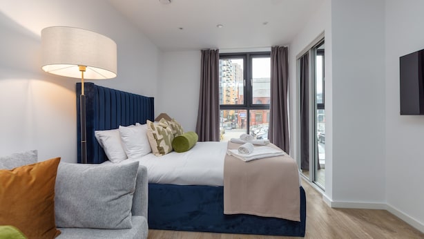 Ein modernes Hotelzimmer mit Bett, Sofa, Lampe und Blick auf die Stadt durch große Fenster.