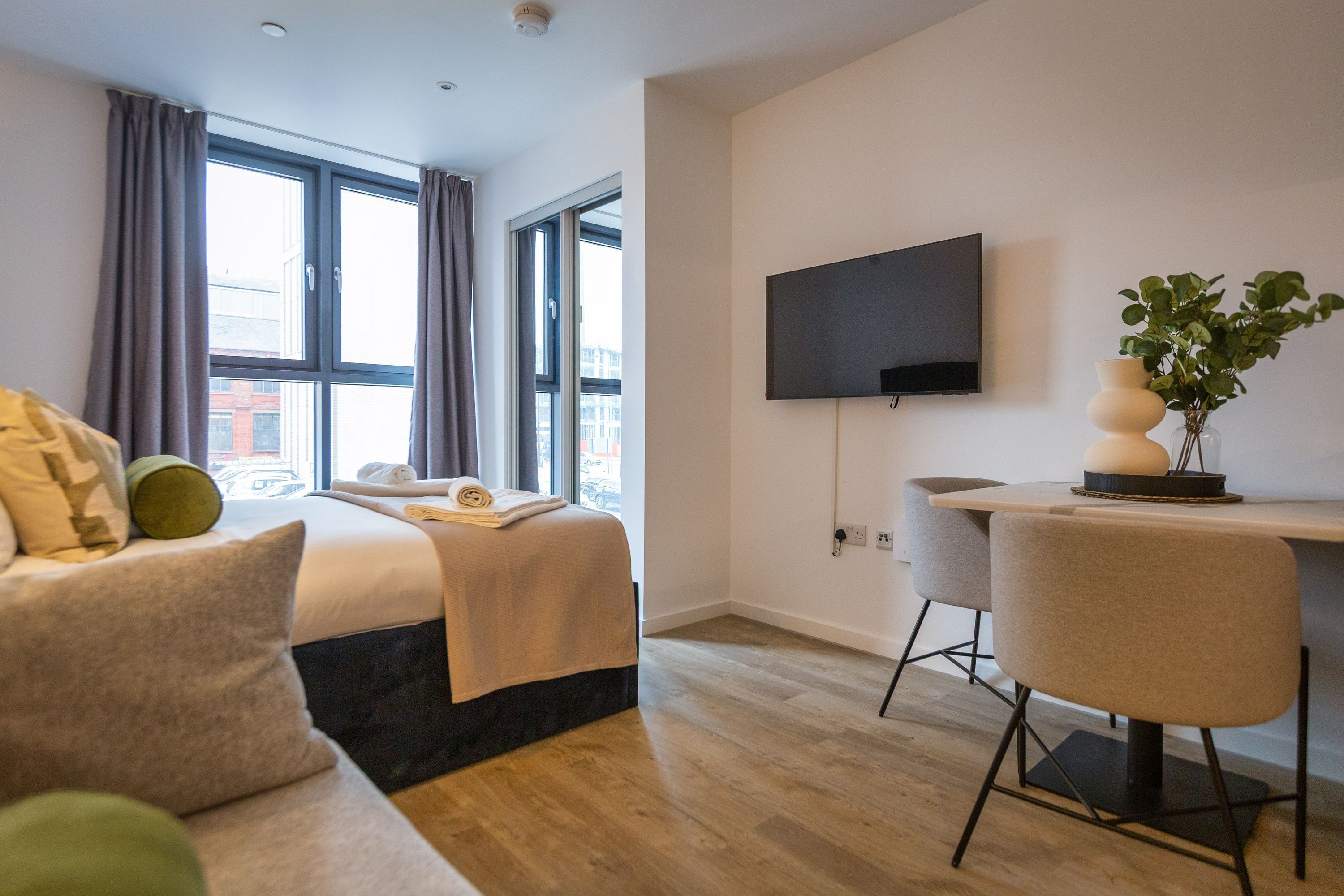 Ett modernt hotellrum med en säng, ett skrivbord, en stol, en TV och ett fönster med gardiner.