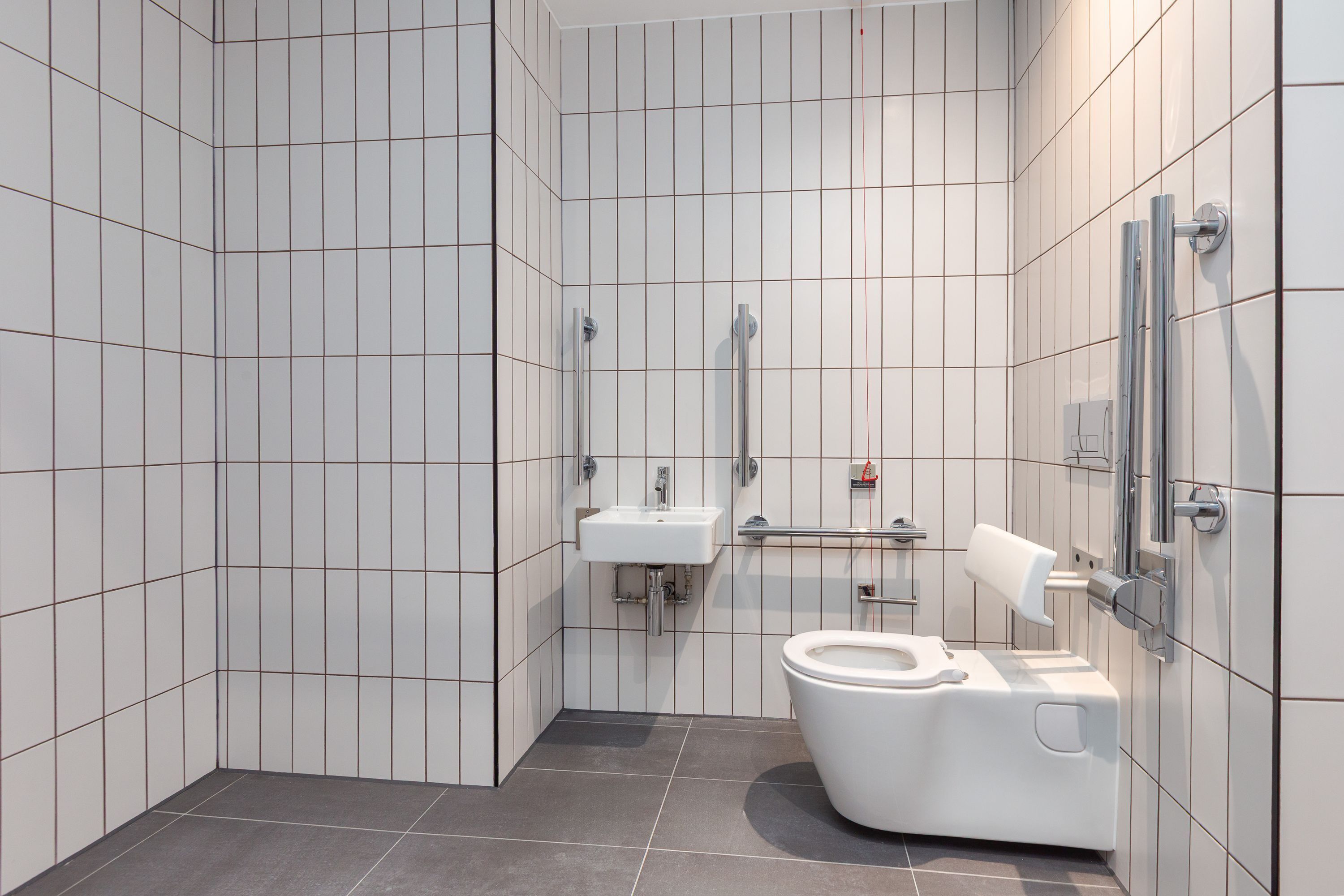 Un baño moderno con paredes de azulejos blancos, inodoro blanco, lavabo y secamanos.