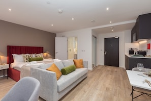 Una habitación de hotel moderna con una cama, sofá gris y una mesa de comedor.