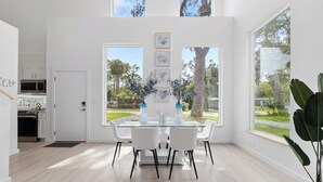 A modern dining area with a glass table, white chairs, and artwork on the wall. - Luxury Modern Comfort in Historic St Augustine (St. Augustine)