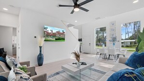 A modern living room with a flat-screen TV, a coffee table, and a dining area with white chairs. - Luxury Modern Comfort in Historic St Augustine (St. Augustine)