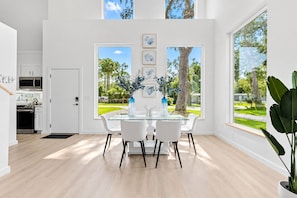 Ein moderner Essbereich mit einem Glastisch, weißen Stühlen und Blick auf einen Garten durch große Fenster.