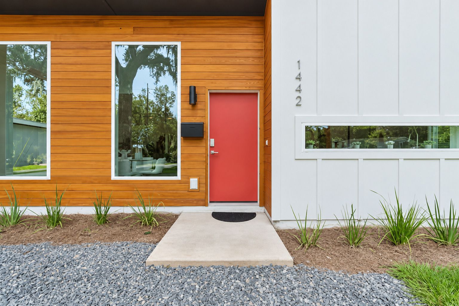 A modern house with a red door, large windows, and a number '1442' on the wall.