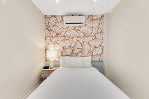 Habitación de hotel con cama, mesita de noche, lámpara y pared con diseño de hojas.