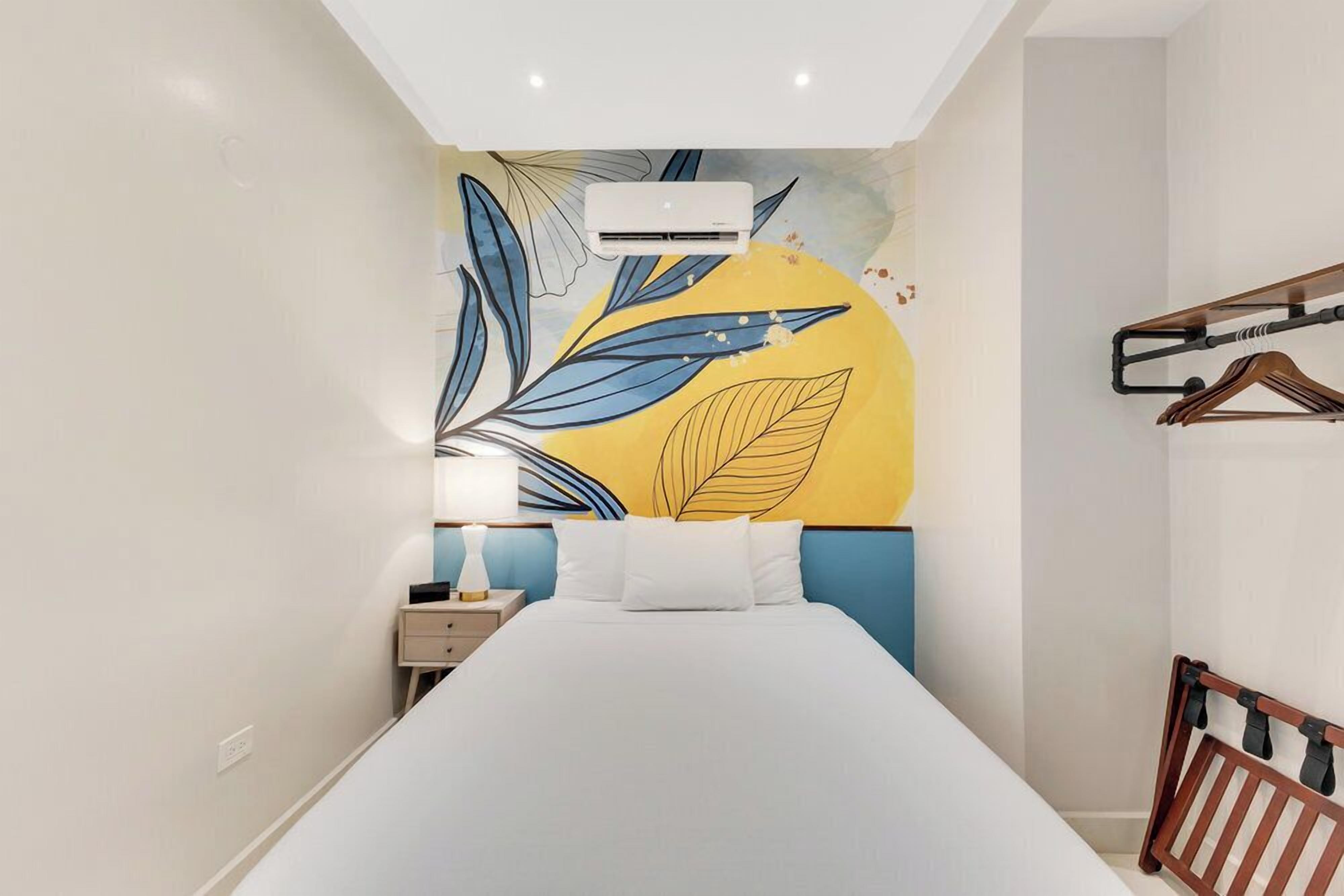 Une chambre d’hôtel moderne avec un grand lit, une table de chevet, une lampe et un climatiseur fixé au mur.