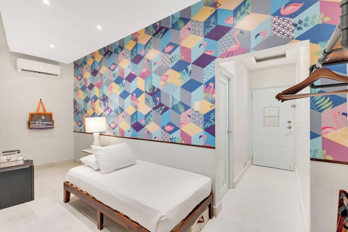 A bedroom with a bed, a bedside table, a lamp, and a colorful geometric-patterned wall.