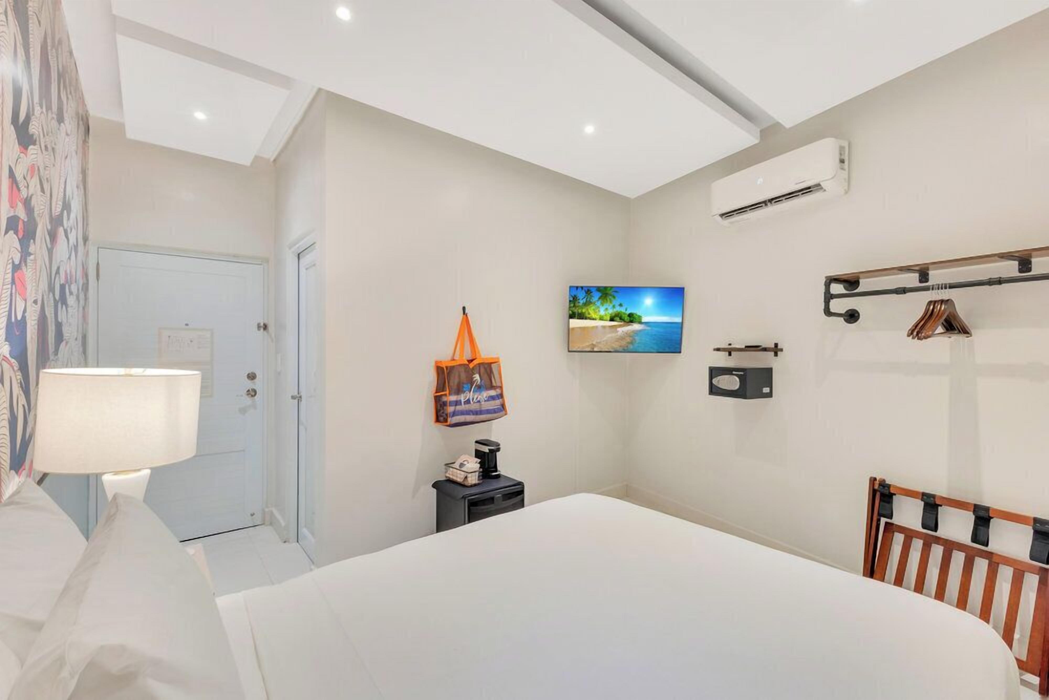 Un dormitorio con cama, mesita de noche, lámpara, televisor y aire acondicionado instalado en la pared.