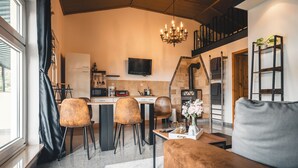A modern kitchen with a flat-screen TV, a stone fireplace, and a dining area with four chairs. - Vacation apartment in the countryside - with lake view, terrace & barbecue fun (Lohmen)