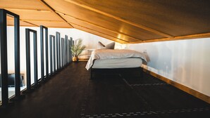 A narrow, high-ceilinged attic bedroom with a bed, a potted plant, and a desk with a lamp. - Vacation apartment in the countryside - with lake view, terrace & barbecue fun (Lohmen)