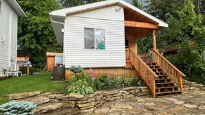 A two-story house with a stone patio, a wooden staircase, and a small garden area.