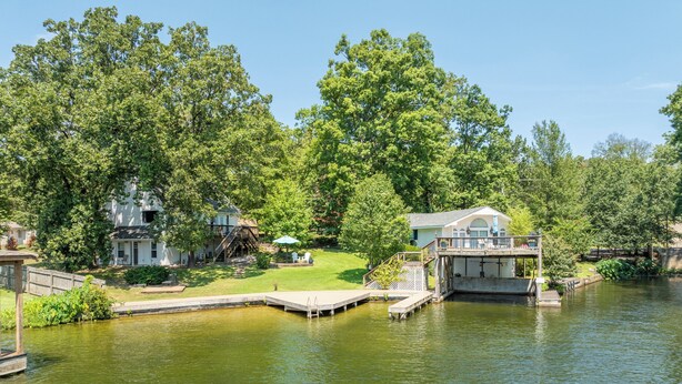 A lakeside property with a dock, a house with a deck, and lush greenery.