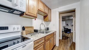 Una cocina con armarios de madera, microondas, estufa, lavaplatos y encimera.