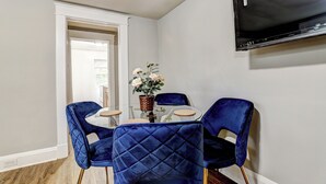 Un rincón comedor con dos sillones de terciopelo azul, una mesa de vidrio y un florero con flores.