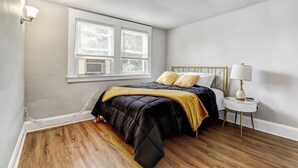 Un dormitorio con cama, mesita de noche, lámpara y ventana con persianas.