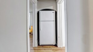 Un pasillo estrecho con un refrigerador blanco en el centro, piso de madera y paredes blancas.