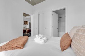 A hotel room with a bed, a brown throw blanket, a white towel, and a patterned pillow.