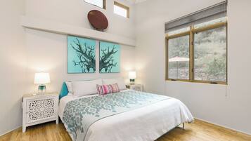 Une chambre à coucher avec un lit, deux lampes fixées au mur, une fenêtre donnant sur un beau paysage et des œuvres d’art accrochées au mur.