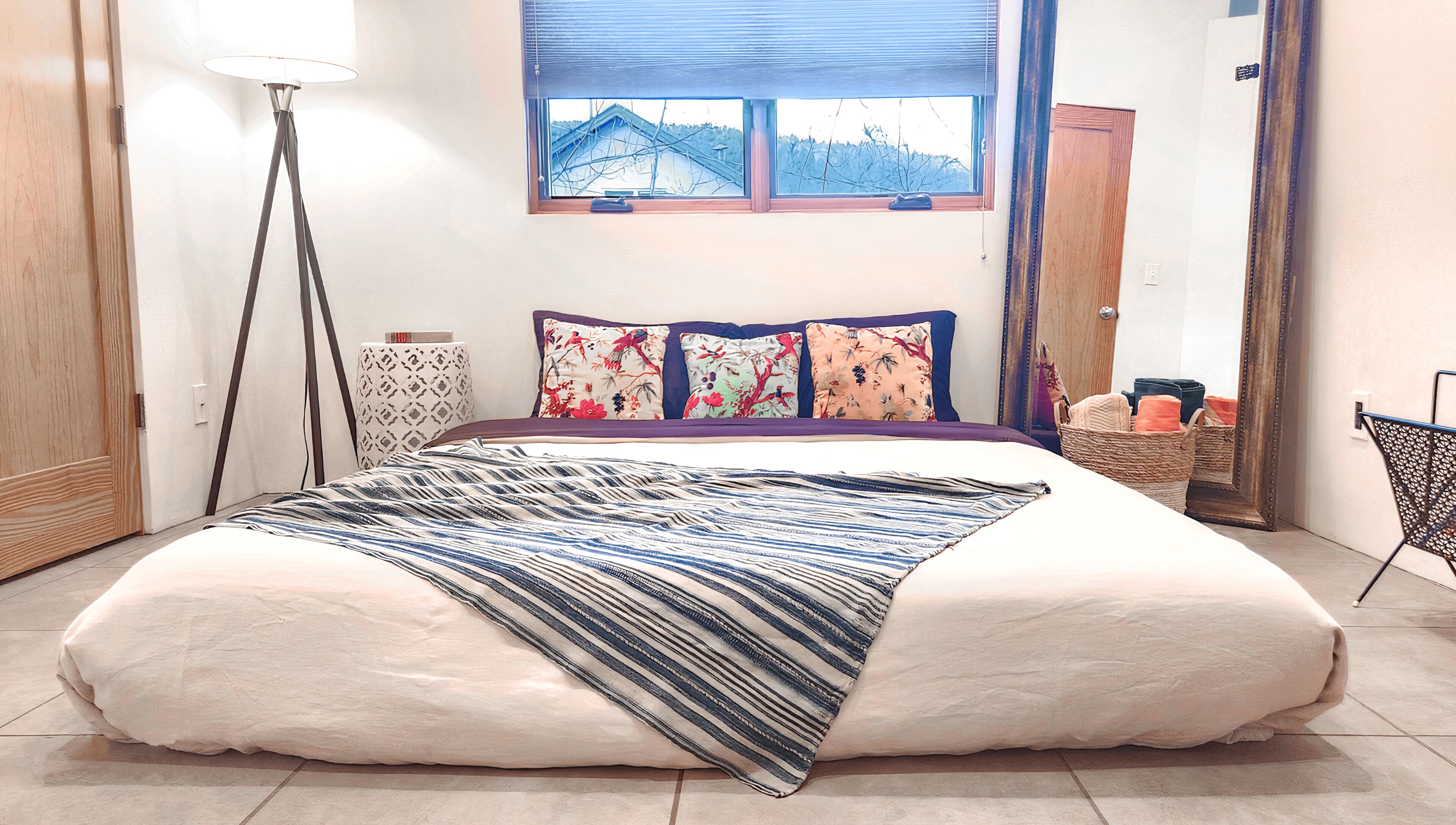 Un dormitorio con una cama grande, una lámpara de pie, una ventana con vistas y un espejo.