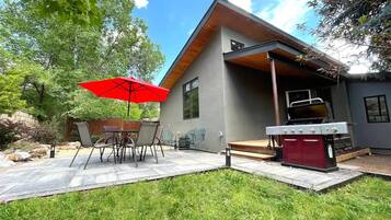 Une maison moderne dotée d’un patio comprenant une table et des chaises, un parasol rouge et un barbecue.