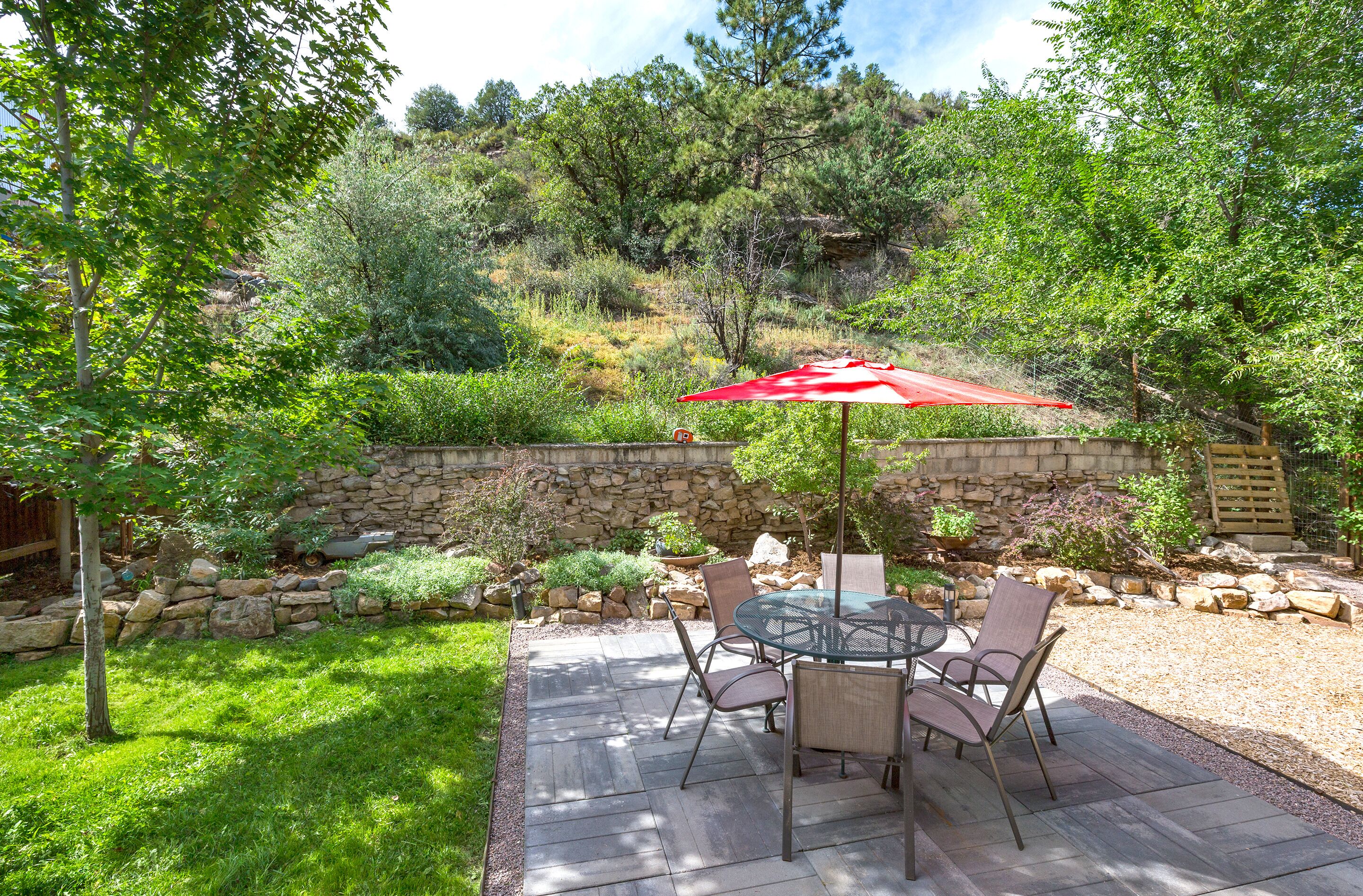 Une terrasse avec un mur en pierre, une table avec des chaises et un parasol rouge.