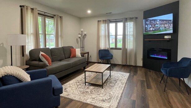 A modern living room with a grey sofa, blue armchairs, a coffee table, and a flat-screen TV mounted on the wall.