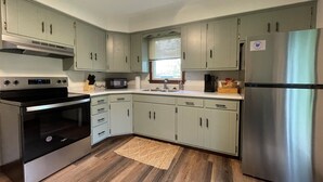 A modern kitchen with light green cabinets, stainless steel appliances, and a wooden floor.