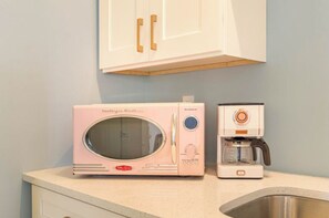 A kitchen with a pink microwave and a coffee maker on the counter.